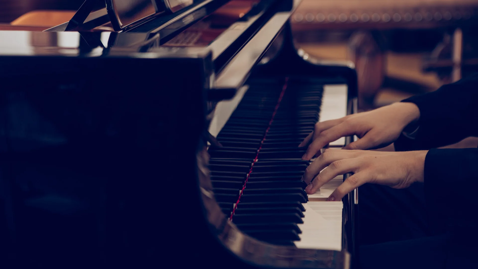 A pianist's hands on the keys of a grand piano in a warmly lit old room